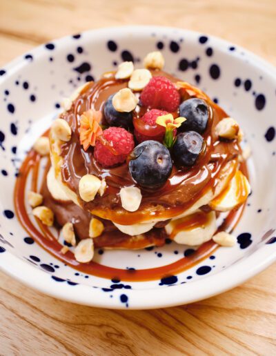 Amerikai palacsinta mogyorókrémmel, karamellszósszal, friss málnával, áfonyával és pirított mogyoróval – Coni Brunch and Bar desszert különlegesség
